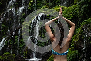 Close up of yoga woman raising arms with namaste mudra in front of waterfall. View from back. Banyu Wana Amertha waterfall