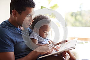 Close up of young adult African American  father reading a book with his two year old son, close up, side view, backlit