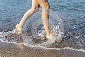 Close-up young adult beautiful slim female barefoot leg girl walking along clear water waves of sea ocean beach shore