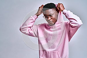 Close up of young african american man in pink streetwear hoodie with hood on head posing isolated on grey background in studio