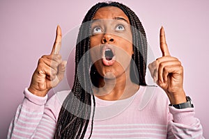 Close up of young african american woman wearing pink sweater over isolated background amazed and surprised looking up and