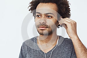 Close up of young african man listening to music in headphones over white background.