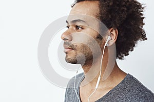 Close up of young african man listening to music in headphones over white background.