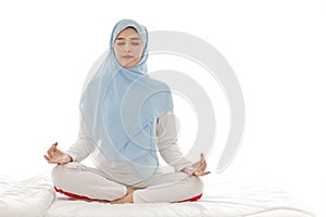 Close up young asian arab woman sitting on bed and enjoying meditation. Beautiful muslim girl in sleepwear with blue hijab