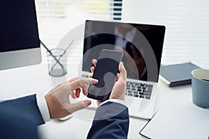 Close-up of a young Asian businessman`s hand holding mobile phone and touching screen on desk in an office. Social networks and