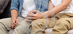 Close up of young asian gay man couple holding hands with happiness while sitting in home living room, homosexual and lgbt