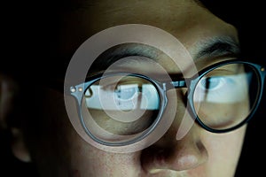 Close up of Young Asian man in glasses watching videos and surfing internet on technology device in the dark.