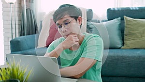 Close-up of a young Asian man in a green shirt, sitting at a laptop screen, with a serious look on his face and a thoughtful