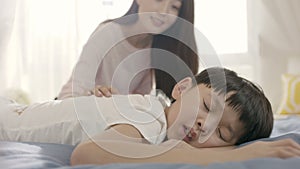 Close up of young Asian mother smiling & waking up her son in morning