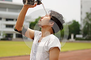 Close up young Asian runner pouring water with waterbottle on his face after running on track.