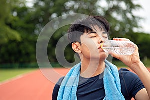 Close up young Asian teenages drinking water from bottle after run in park with copy space