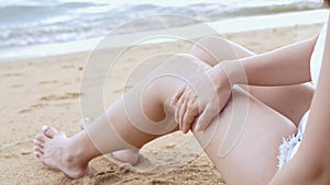 Close up Young asian woman applying a sunscreen or sunblock lotion on leg her skin on a seaside beach tropical resting and relaxat