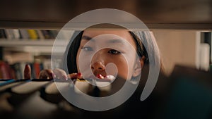 Close-up young asian woman browsing shelves books concentrated female student looking for necessary book to read on