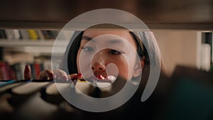 Close-up young asian woman browsing shelves books concentrated female student looking for necessary book to read on