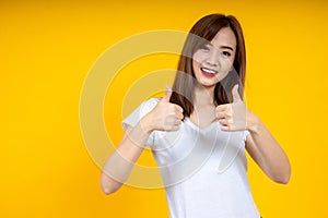 Close up of young Asian woman isolated on yellow background showing thumps up