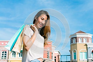 Close up of a young Asian woman shopping an outdoor flea market with a background of pastel bulidings and blue sky.