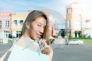 Asian woman shopping an outdoor flea market with a background of pastel bulidings and blue sky.