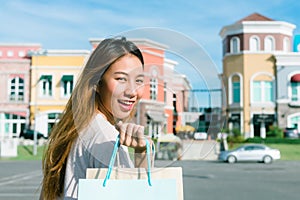 Close up of a young Asian woman shopping an outdoor flea market with a background of pastel bulidings and blue sky.