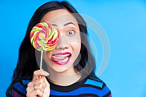 Close up of young asian woman sticking out tongue covering her eye with colorful lollipop