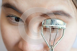 Close-up of young Asian woman using eyelash curler.