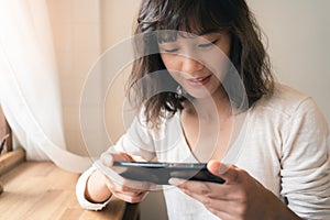 Close up of young Asian woman using smartphone watching video clip and playing online game. A happy female with smiley face.