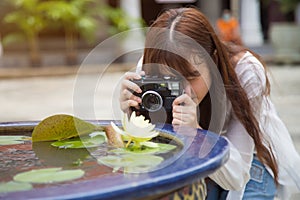 Close up young Asian woman in a white shirt taking a photo by camera to a water lilly in a pond while travelin in Asia
