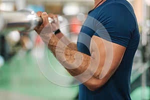 Close up of young athlete trains in the gym. Trians biceps muscules using barbell