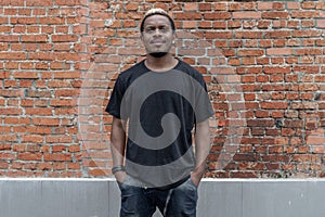 Young attractive dark-skinned man in black T-shirt on red bricked background.