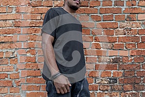 Young attractive dark-skinned man in black T-shirt on red bricked background.