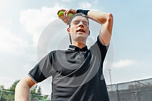 Close up of young man relaxing after tournament and holding tennis balls.