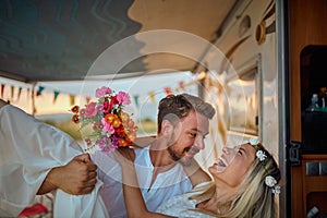 close up of a young beardy man carrying his bride inside of the camper, smiling, laughing