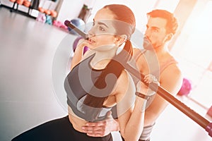 Close up of young and beautiful boy and girl exercising in gym. She is doing some squads using bodybar while her trainer