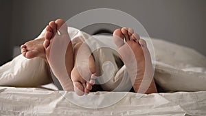 Close up of young beautiful and loving couple lying on the bed. Their feet under blanket while wake up in bed in morning