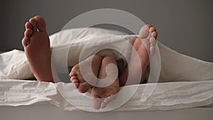 Close up of young beautiful and loving couple lying on the bed. Their feet under blanket while wake up in bed in morning