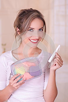 Close up of a young beautiful smiling woman holding a menstruation cotton tampon in her hand and a colorful purse inn