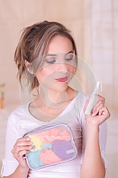 Close up of a young beautiful smiling woman holding a menstruation cotton tampon in her hand and a colorful purse inn