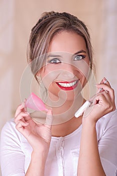 Close up of young beautiful smiling woman holding a menstruation cotton tampon in one hand and with her other hand a