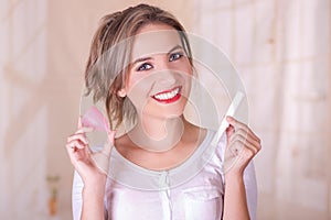 Close up of young beautiful smiling woman holding a menstruation cotton tampon in one hand and with her other hand a