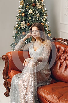 Close up of young beautiful woman sit on brown sofa near festive Christmas Tree