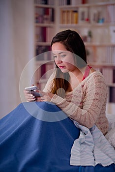 Close up of young beautiful woman with sleeplessness sitting on the bed using her cellphone, insomnia concept