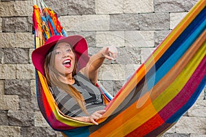 Close up of young beautiful woman wearing a red fashion hat and relaxing in a hammock, pointing somewhere with her arm