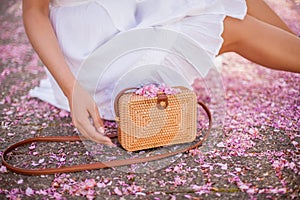 Close-up. A young beautiful woman in a white dress is holding a wicker bag. Sakura. Blooming trees