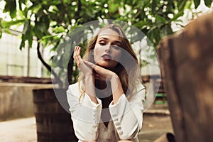 Close up young beautiful woman in white jacket and dress dreamily looking in camera while spending time in cozy garden
