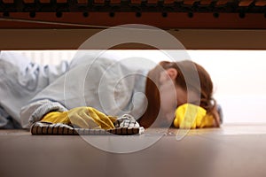 Close up of young beautiful woman with yellow rubber gloves and rag is cleaning floor under bed at home. Concept of