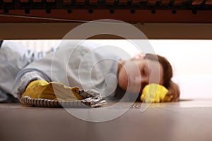 Close up of young beautiful woman with yellow rubber gloves and rag is cleaning floor under bed at home. Concept of