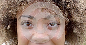 Close-up of a young biracial woman with curly hair and a subtle smile