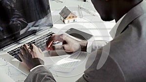 Close up of young black businessman hands typing on laptop computer keyboard in white modern office in the sunny day