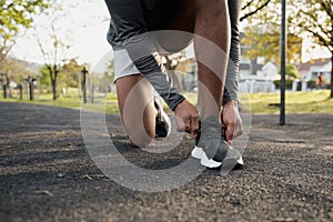 Close-up of young black man in sports clothing kneeling while tying shoelace in park