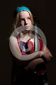 Close up of young blonde girl hugging a violin on a black studio background