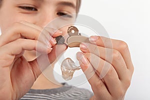 Close up of a young boy`s hands replacing a battery of a hearing aid with open batter compartment